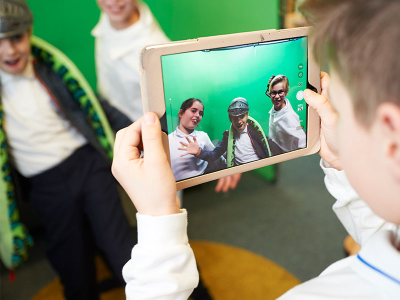 Boy filming class mates in fancy dress on tablet